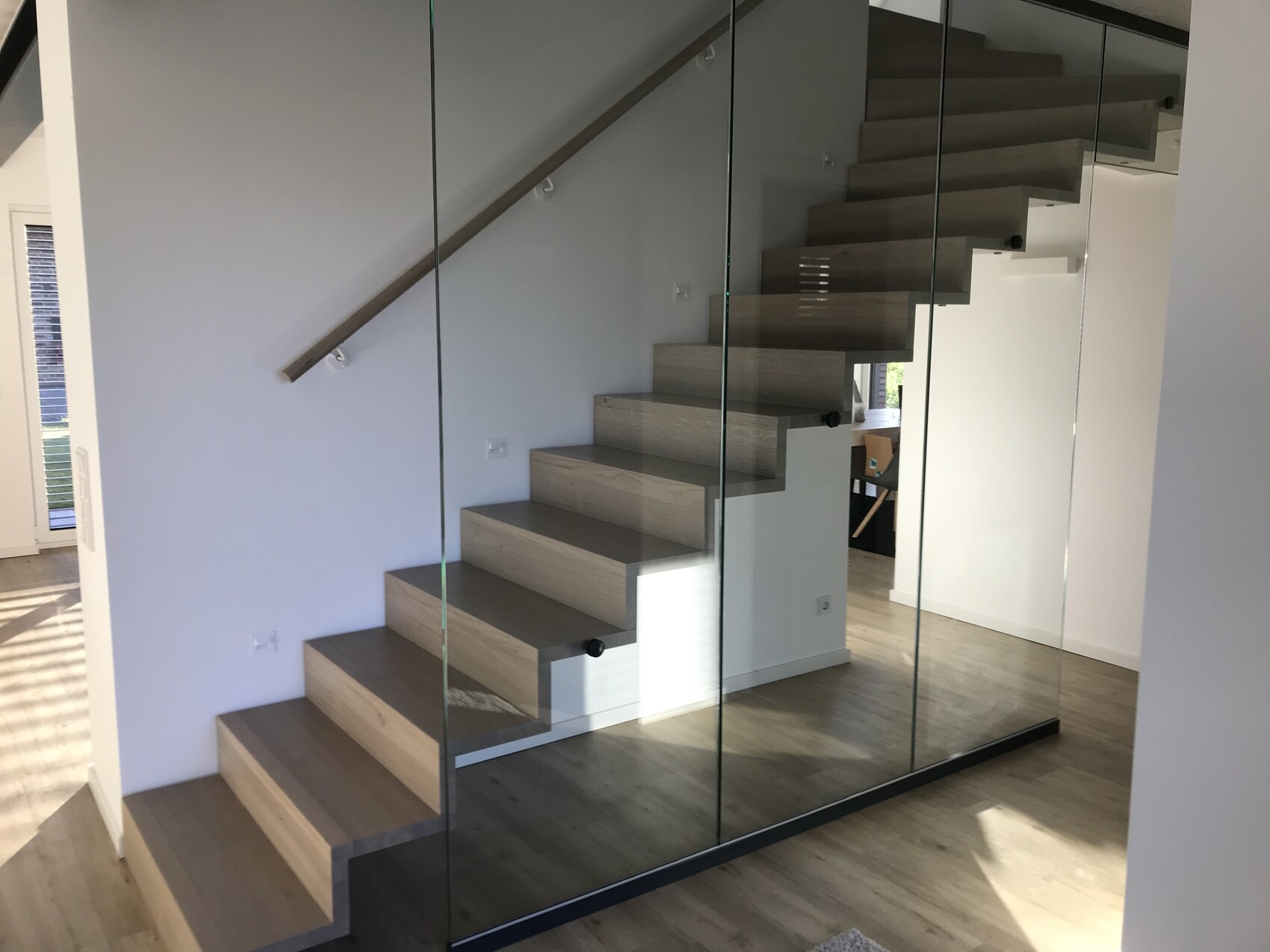 Moderne, schwebende Holztreppe mit Glaswand und Spiegel in hellem Wohnraum.