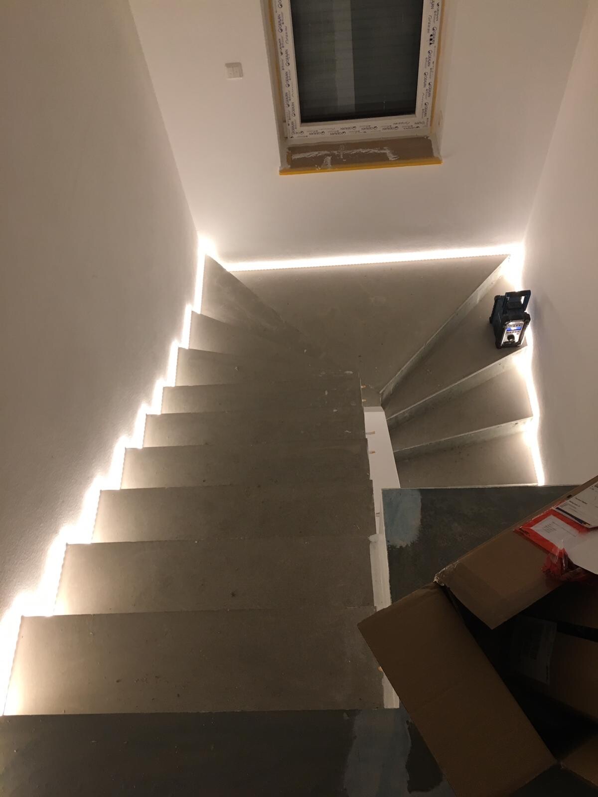 Stufen einer Treppe im Bau, LED-Lichtleisten an den Kanten, Kartons rechts.