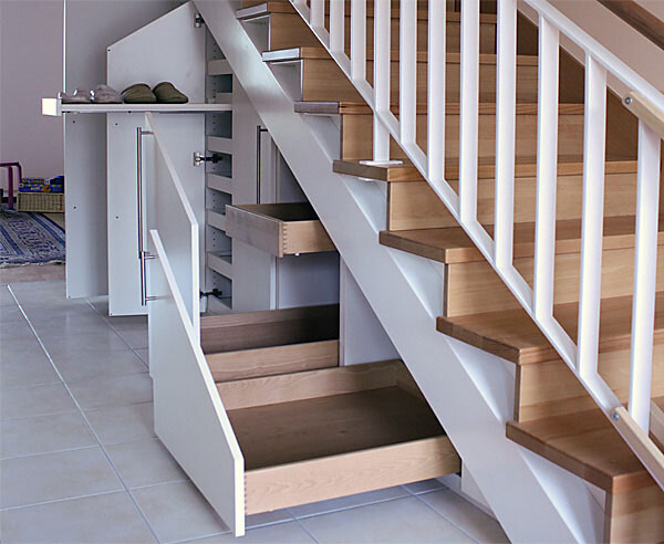 Unter der Treppe offenes Stauraumsystem mit Schubladen und Türen, Holzstufen, Weißes Geländer.