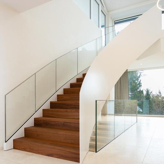 Moderne Innentreppe aus Holz mit Glasgeländern und einer weißen Kurve im hellen Raum.