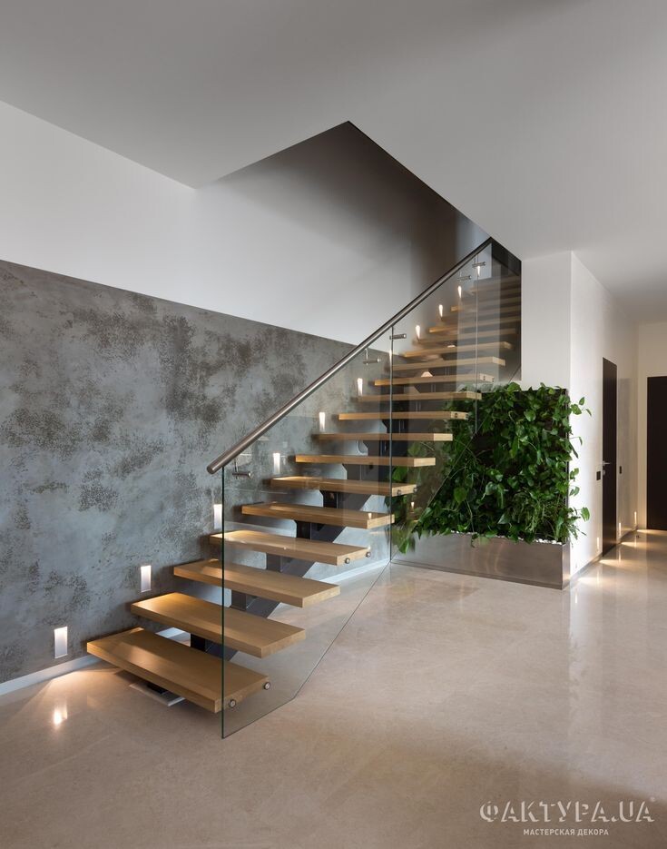 Moderne Treppe mit Holzstufen und Glasgeländer, Betonwand links, Pflanzenwand rechts.