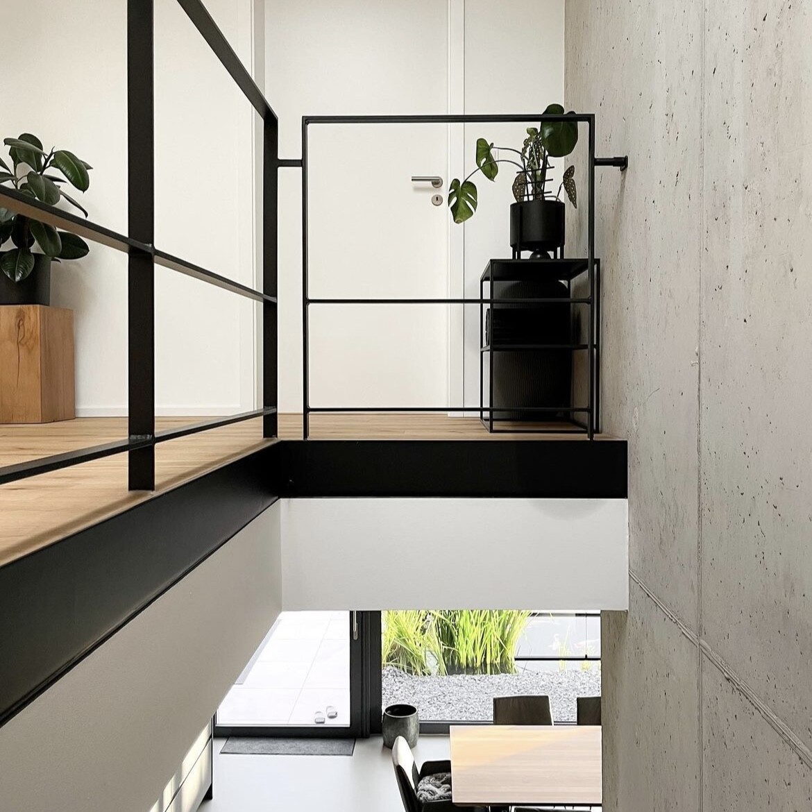 Moderne Loft-Galerie mit schwarzem Metallgeländer, Pflanzentopf und Holzboden.