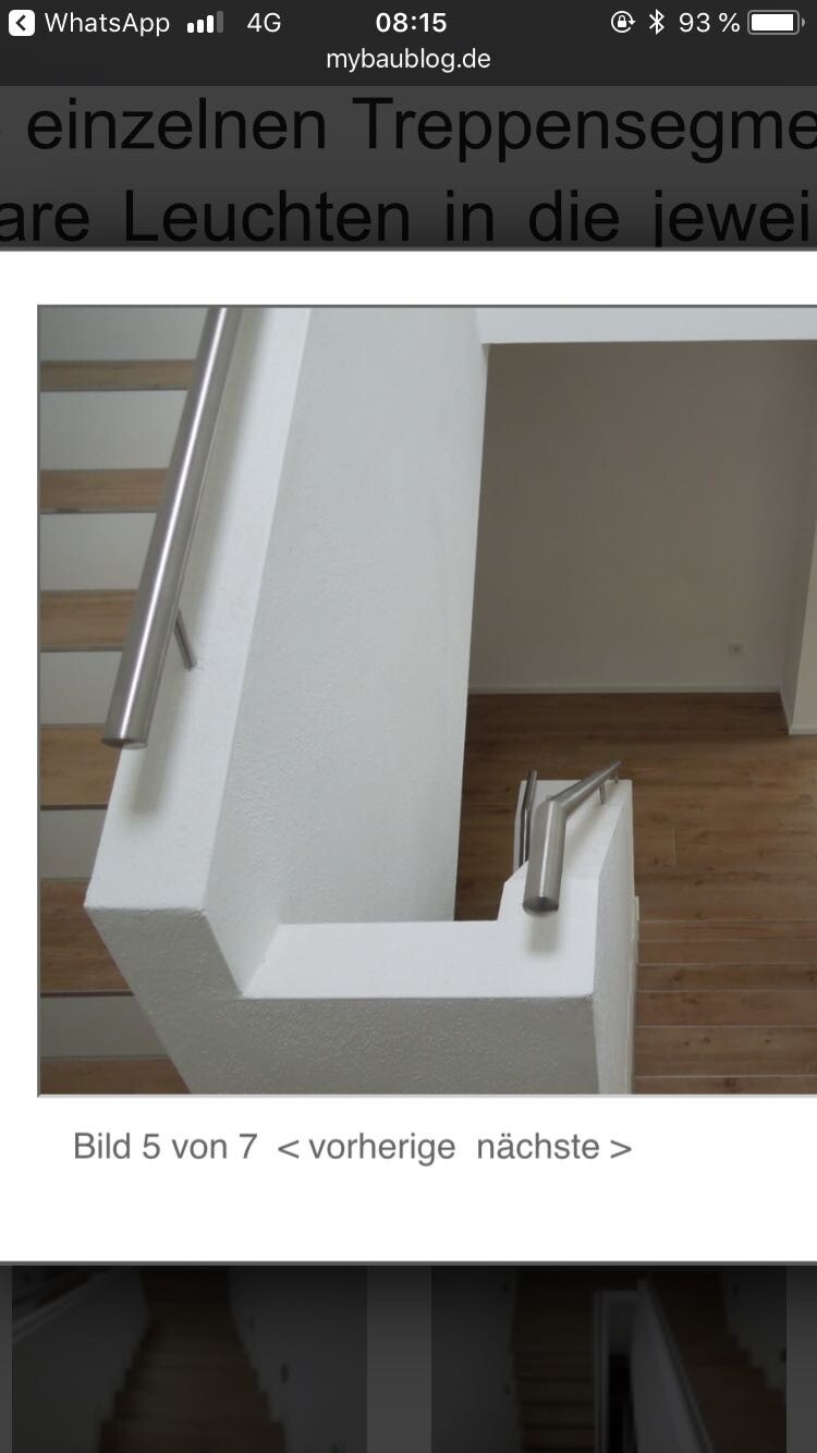 Innenraum-Treppenaufgang mit weißer Betonbrüstung, Edelstahlhandlauf und Holzstufen.