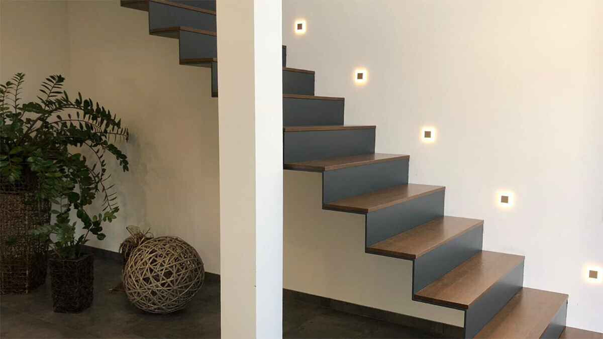 Moderne Innentreppe aus Holz, weiße Wand, kleine quadratische LEDs, Topfpflanze und Korbdekoration.