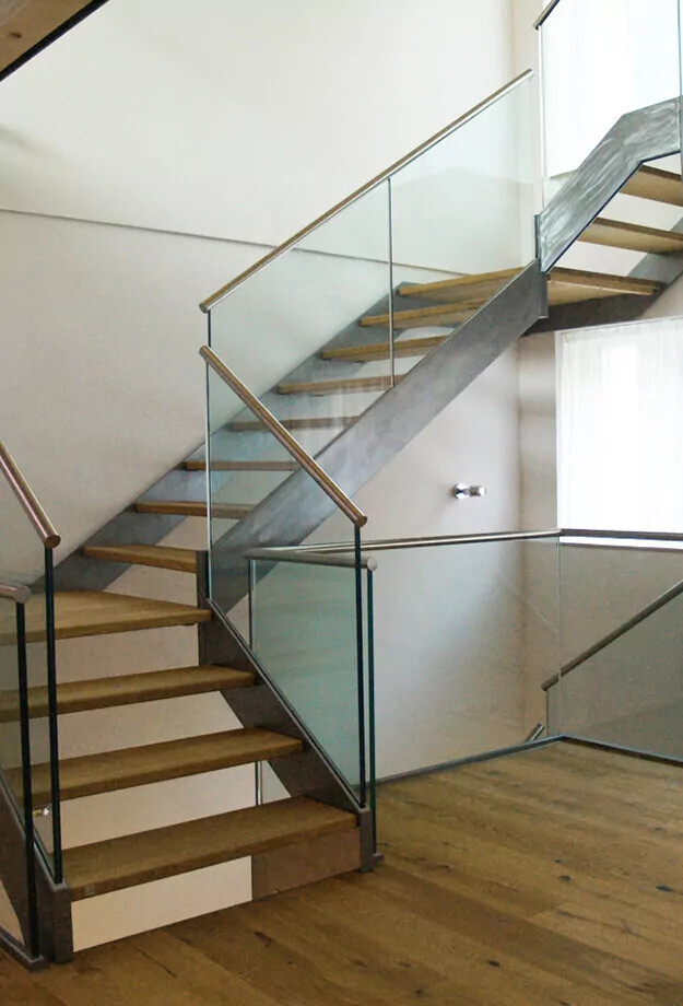 Moderne Treppe mit Holzstufen, Glasgeländer und Metallrahmen in hellem Innenraum.