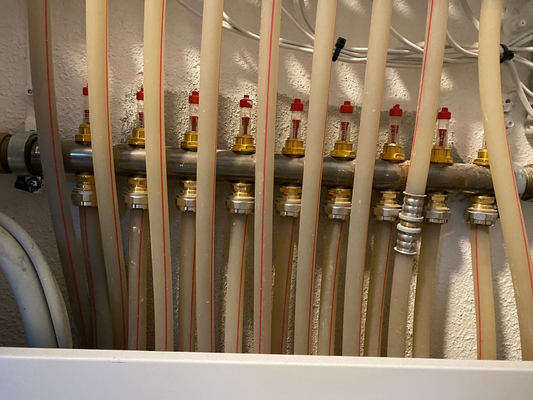 Verteiler mit mehreren Schlauchleitungen und Messingventilen vor einer Wand.
