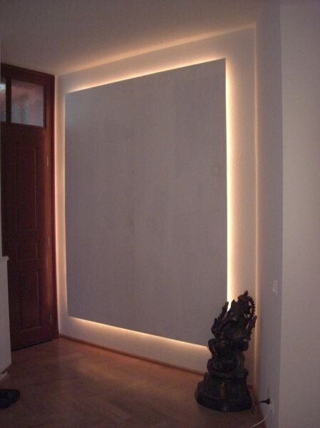 Großes, rechteckiges Wandpaneel mit LED-Beleuchtung an der Wand; Skulptur unten rechts.