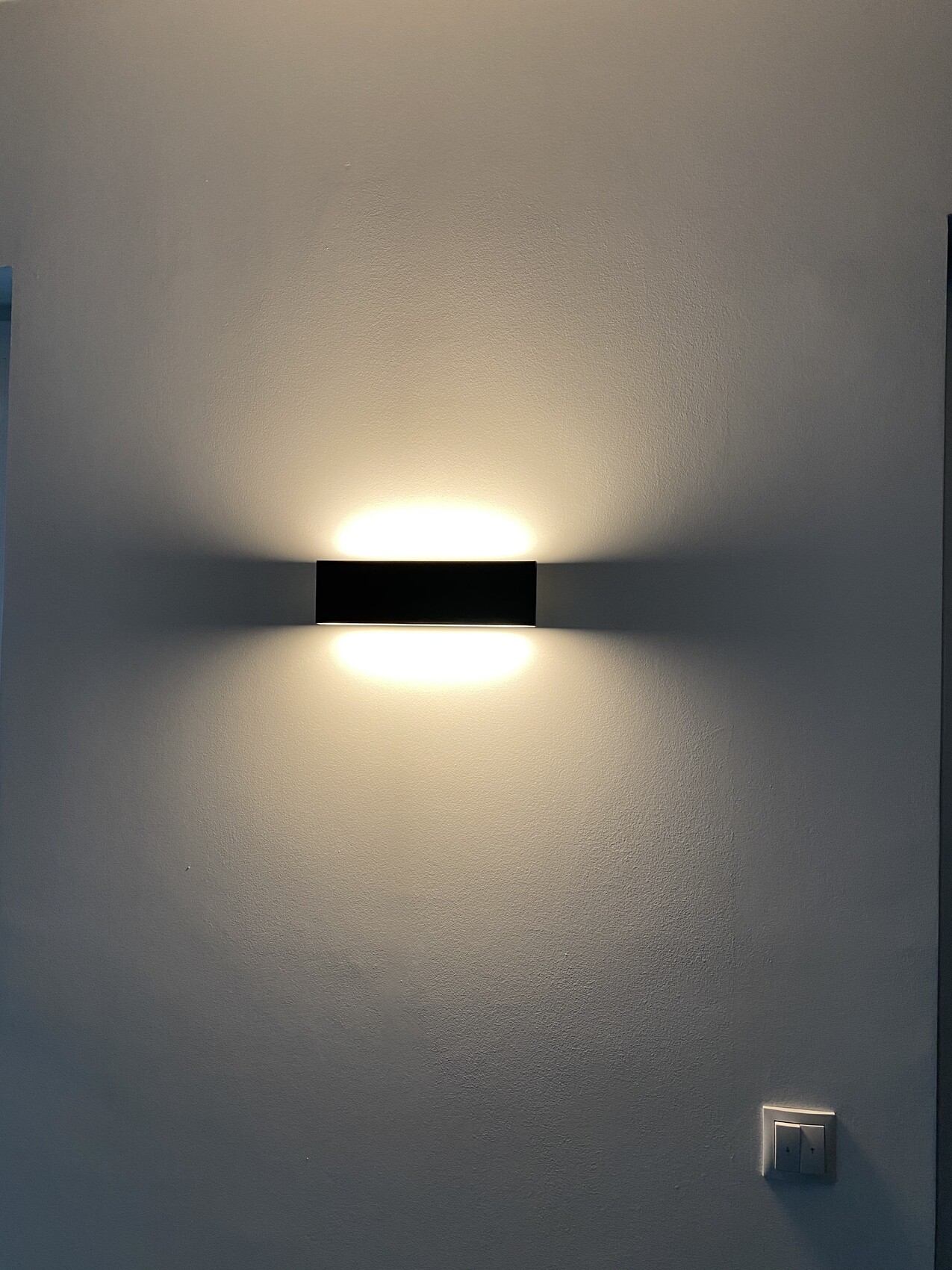Schwarze horizontale Wandlampe an heller Wand, Licht nach oben und unten strahlend.