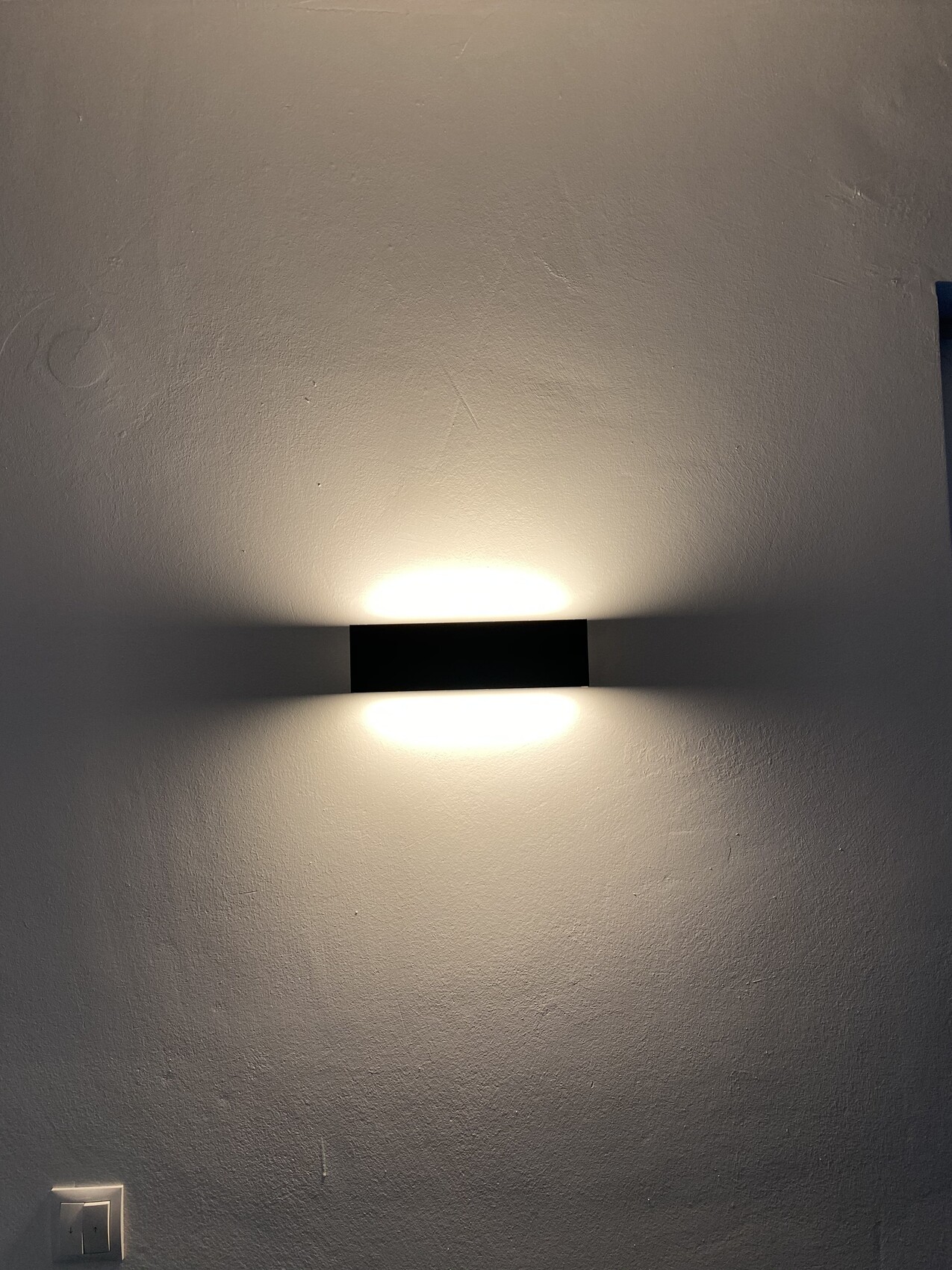 Schwarze rechteckige Wandlampe an heller Wand; Licht strahlt oben und unten aus.