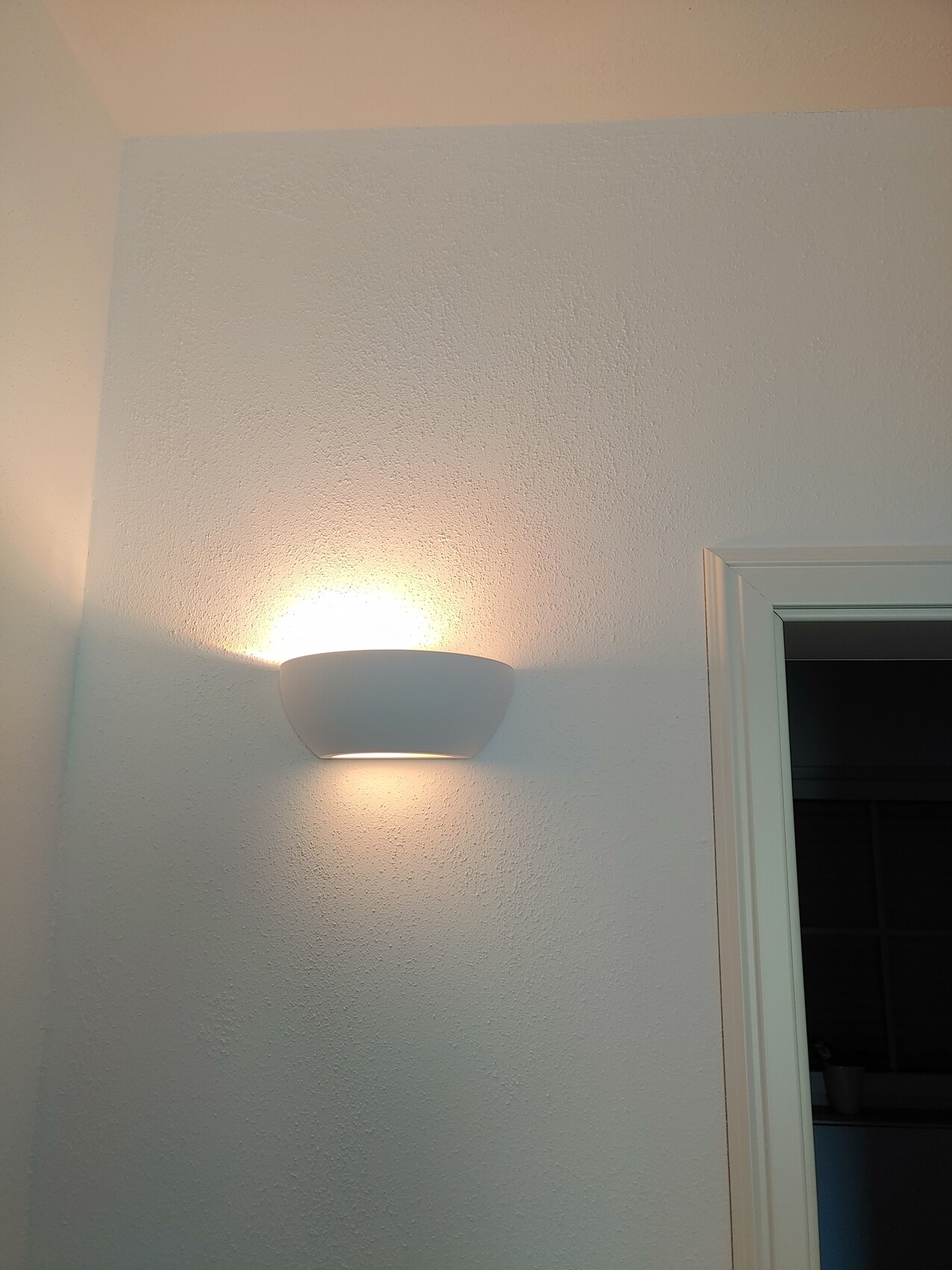 Weiße halbkugelige Wandlampe an heller, texturierter Wand; warmes Licht oben/unten.