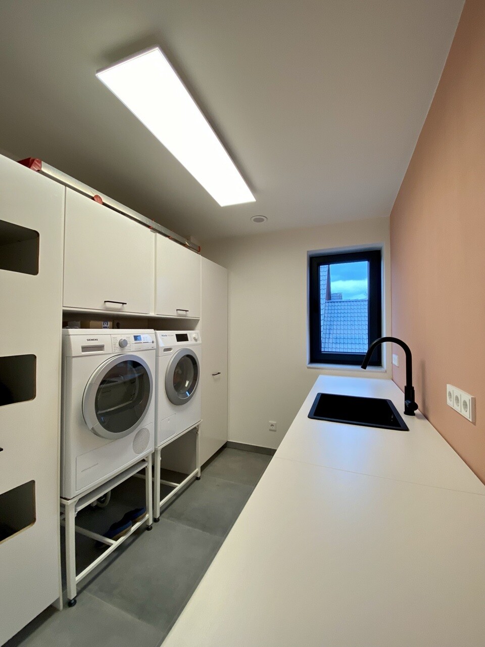 Moderne Waschküche: weiße Schränke, Waschmaschine & Trockner, Spüle, Fenster.