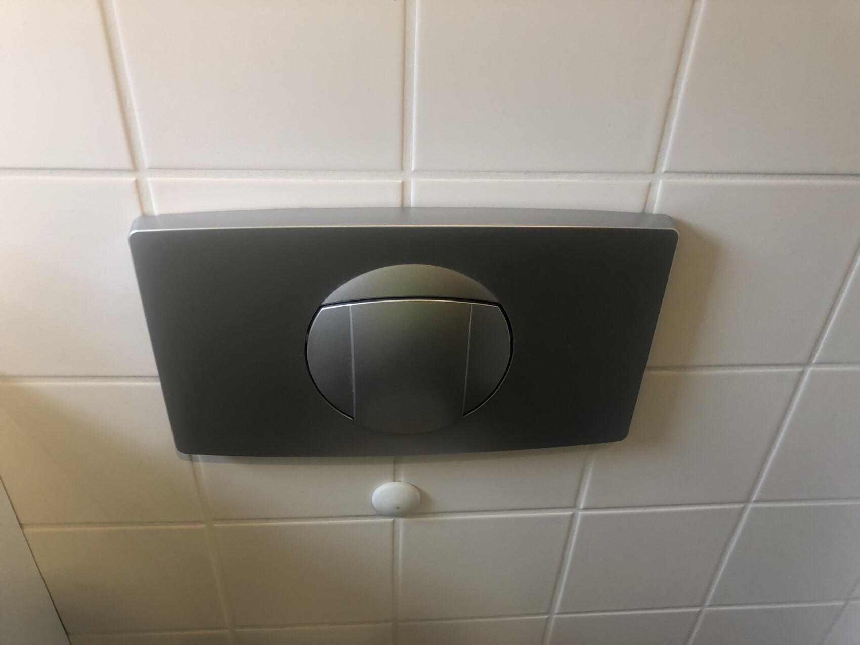 Wandmontierte schwarze Spülplatte mit rundem Knopf auf Fliesen.