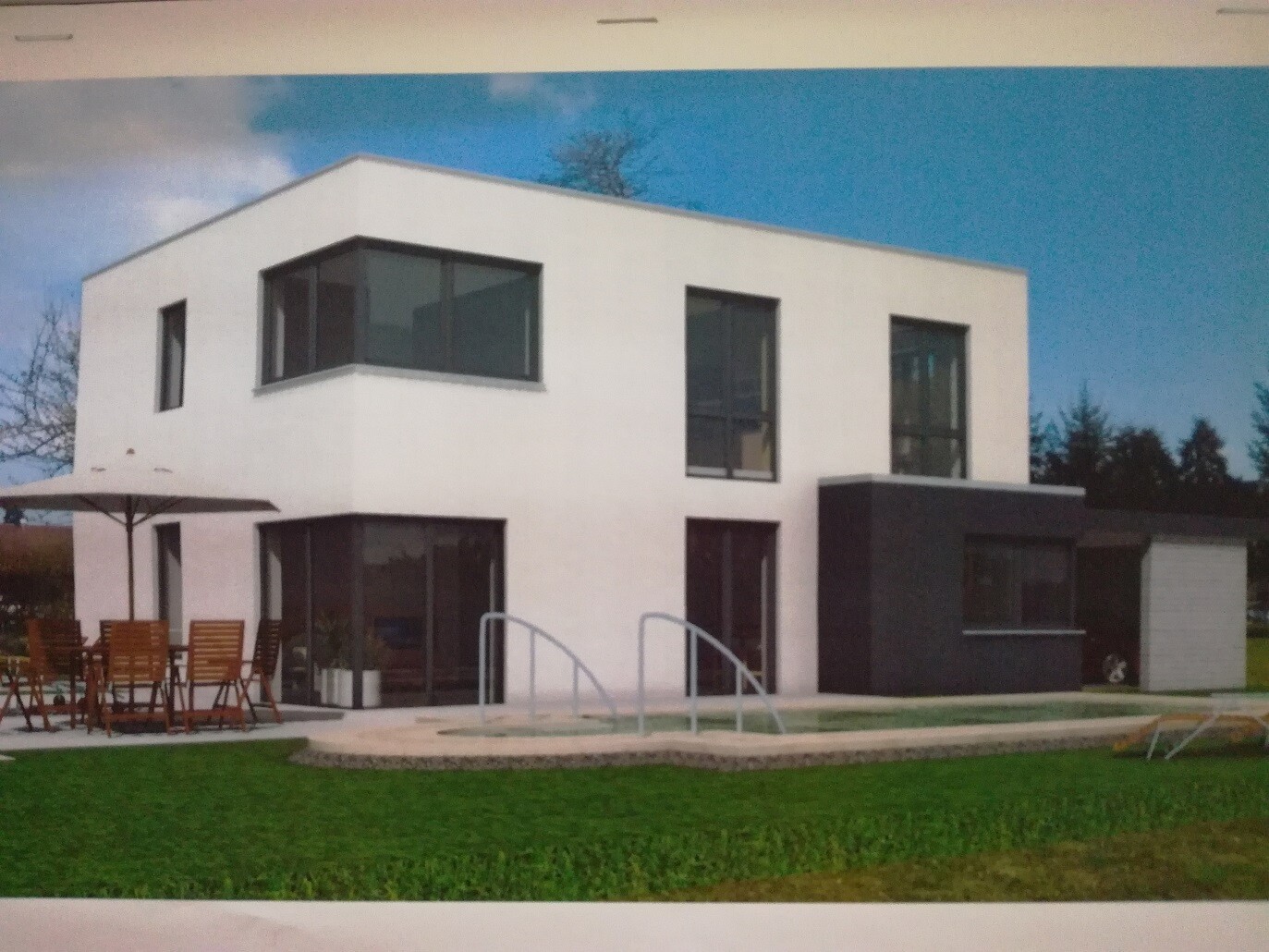 Moderne weiße zweistöckige Villa mit großen Fensterfronten, dunklem Anbau, Gartenmöbeln und Grünfläche.