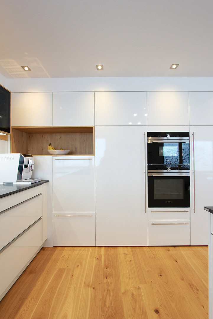 Moderne Küche mit weißen Hochglanz-Schränken, Doppel-Backofen und Holzfußboden.