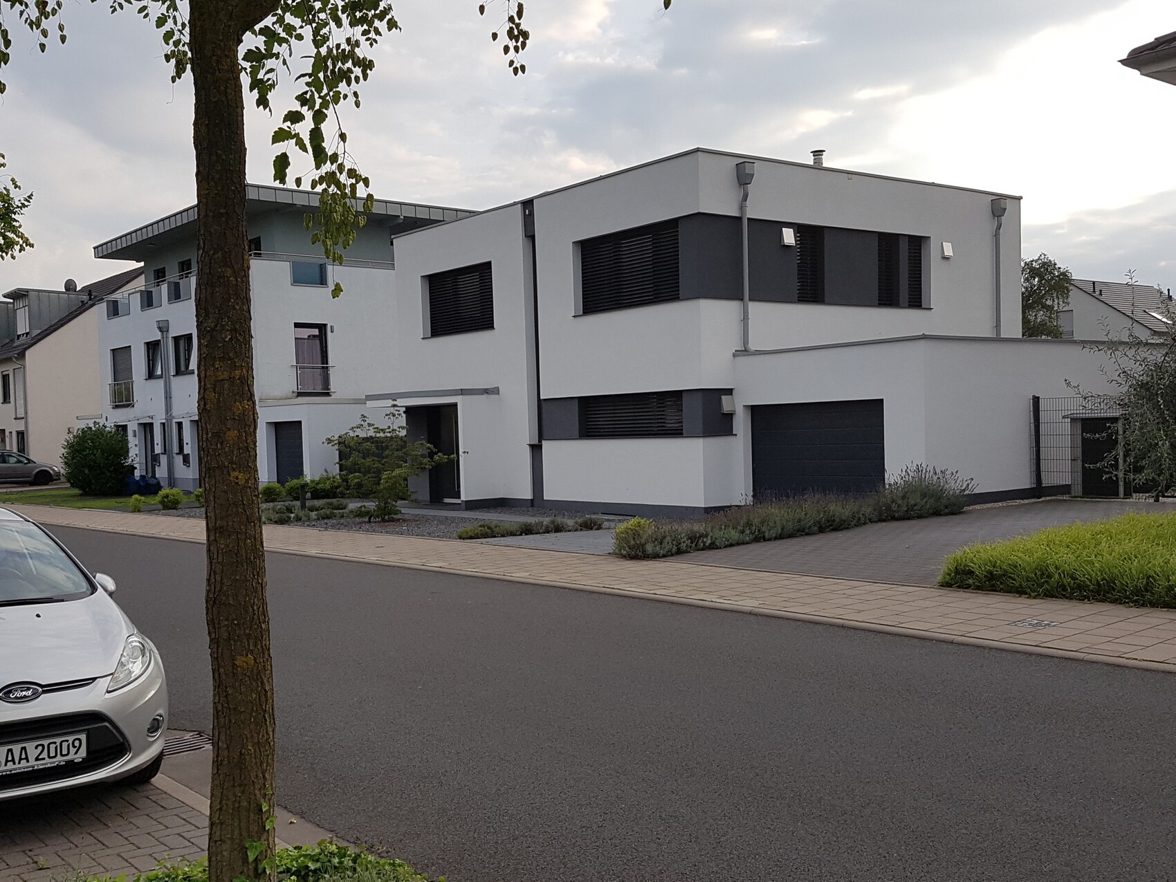 Moderne Wohnsiedlung mit weißen Gebäuden, Garage, Gehweg und geparktes Auto am Straßenrand.