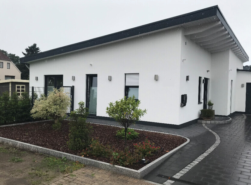 Modernes weißes Einfamilienhaus mit Gartenbeet, gepflasterter Zufahrt.