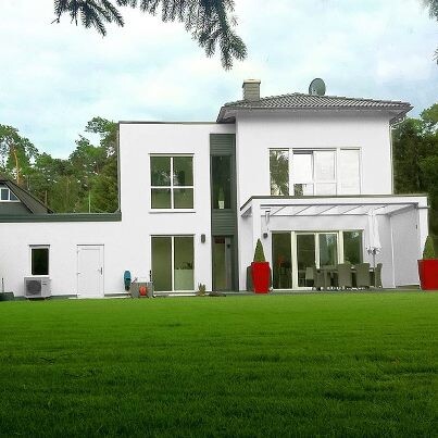 Moderne weisse Haus-Aussenansicht mit Terrasse und gruenem Garten