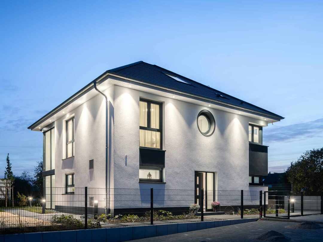 Moderne zweistöckige weiße Villa mit runder Fensteröffnung, Außenlampen und Zaun.