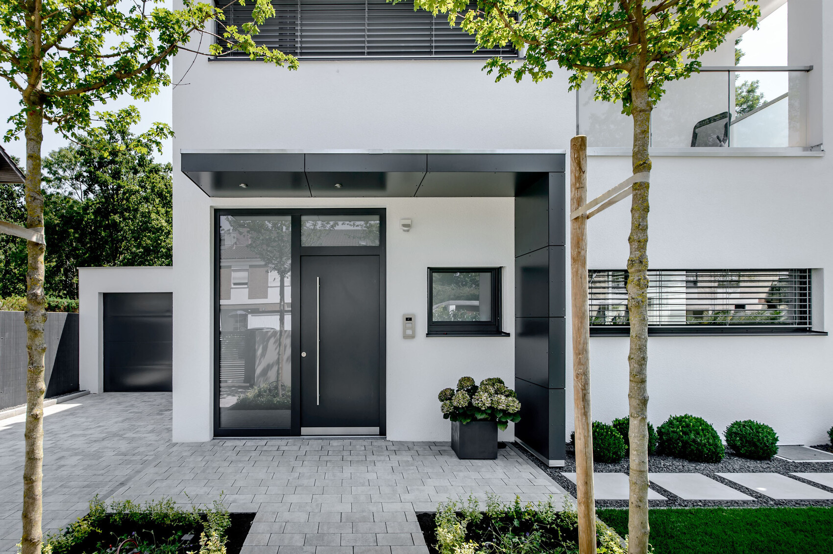 Modernes weißes Wohnhaus mit dunkler Eingangstür, kleinem Fenster, Garage links, Pflanzkübel.