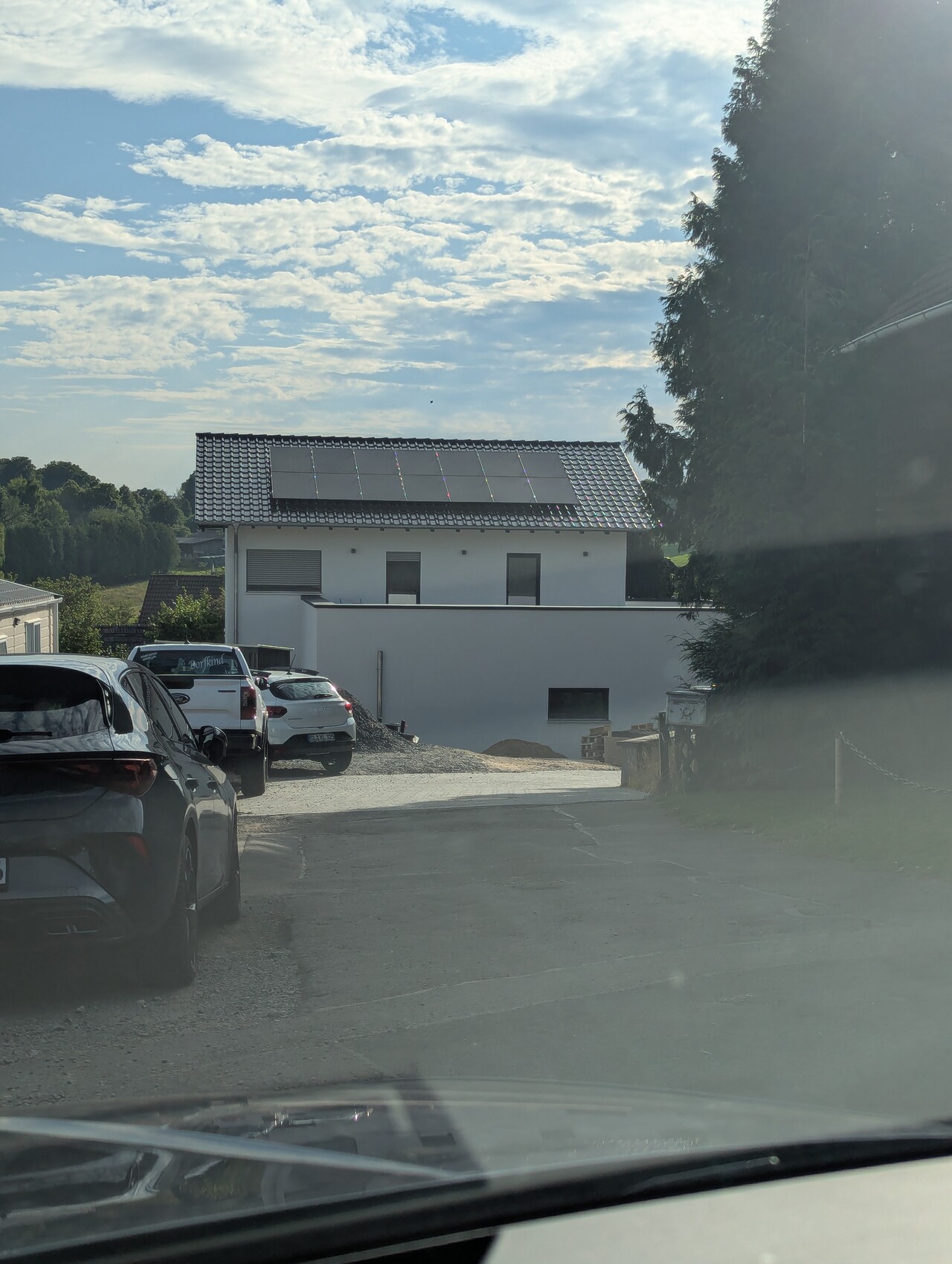 Weißes modernes Haus mit Solaranlagen auf dem Dach; davor eine Reihe geparkter Autos.