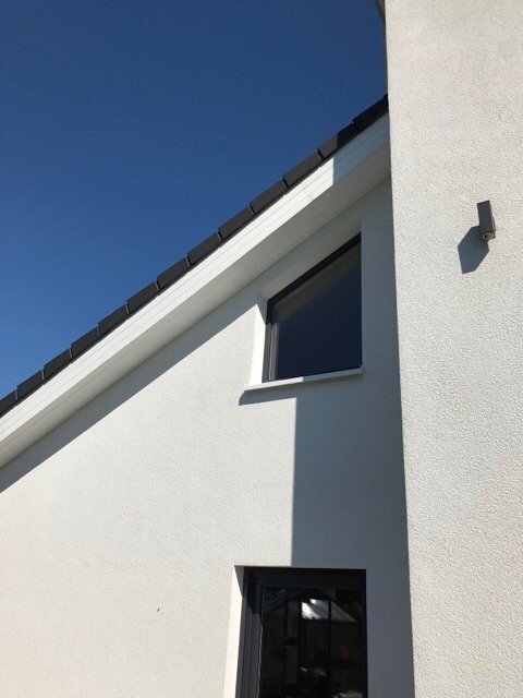 Weiße Fassade mit schrägem Dach, Fenster und Schatten, blauer Himmel im Hintergrund