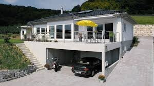 Außenansicht eines modernen weißen Hauses mit Terrasse, gelbem Sonnenschirm und Garage darunter.