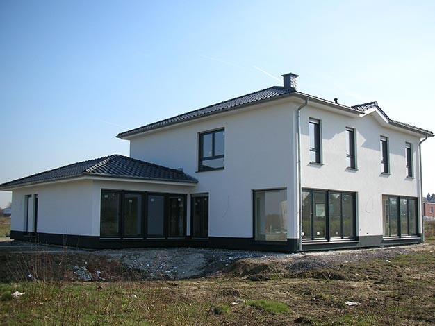 Modernes weißes Einfamilienhaus mit großen Fenstern und dunklem Sockel auf Bauland