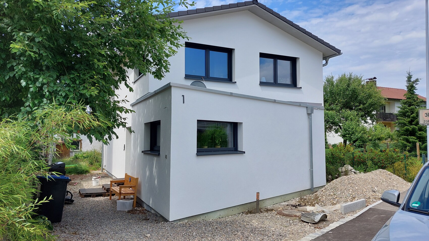 Weißes modernes Haus, zwei Stockwerke, dunkle Fensterrahmen; Bau- und Gartenbereich mit Kies.