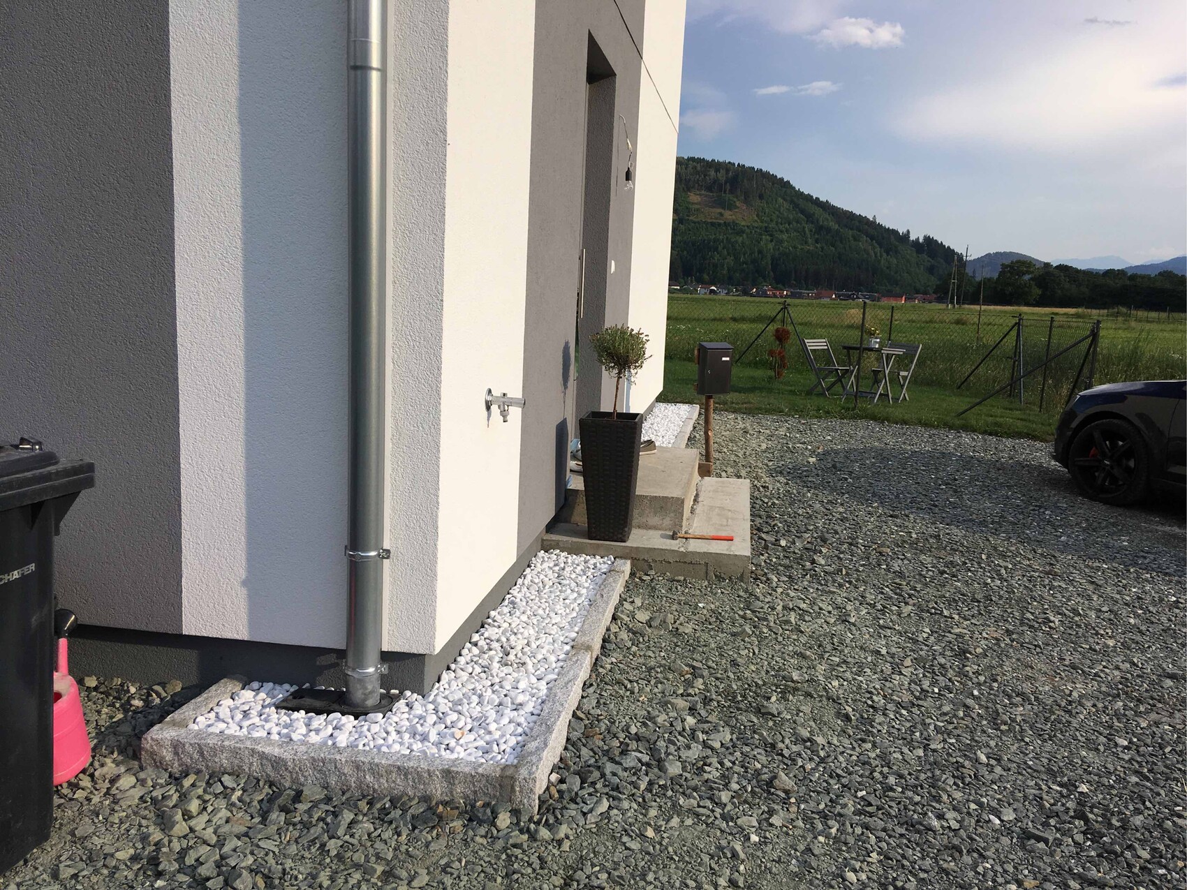 Außenansicht eines modernen Hauses mit Pflanzkübel, Regenrohr, Kiesweg und geparktes Auto.