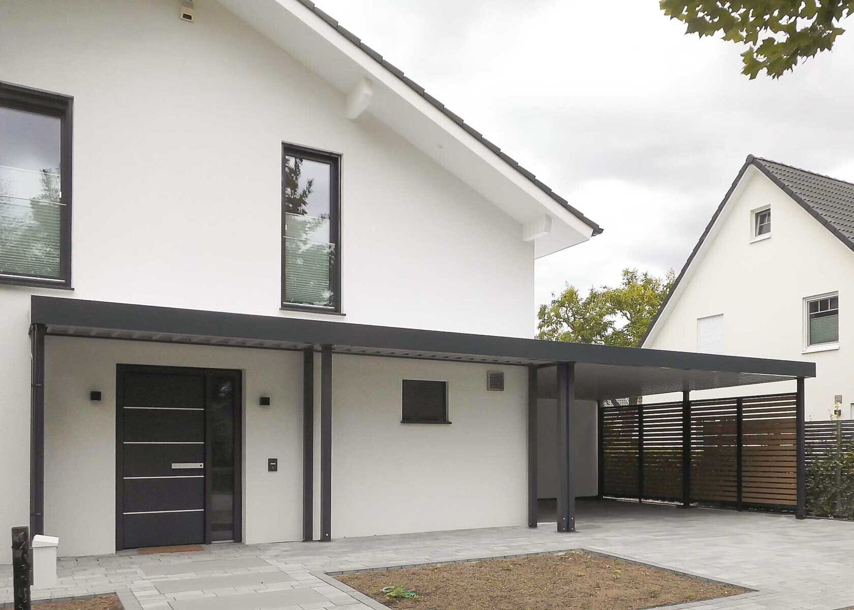 Moderne weiße Hausfront mit schwarzem Carport und dunklem Eingangstor, seitlicher Holzzaun.