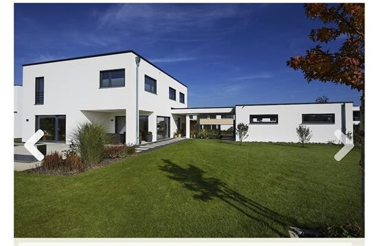 Modernes weißes Wohnhaus mit großer Rasenfläche und blauem Himmel.