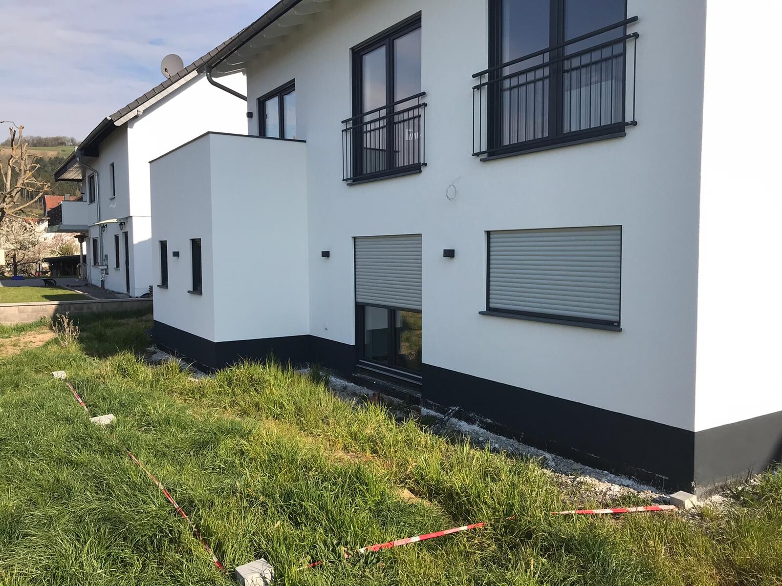 Modernes weißes Wohnhaus mit schwarzen Balkonen und Rollläden; Gras im Vordergrund