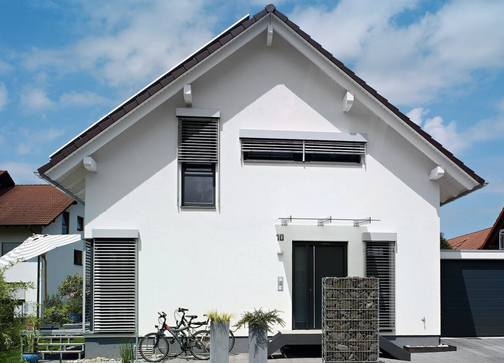 Modernes weißes Einfamilienhaus mit Satteldach, Fensterjalousien und Fahrrädern vor dem Eingang