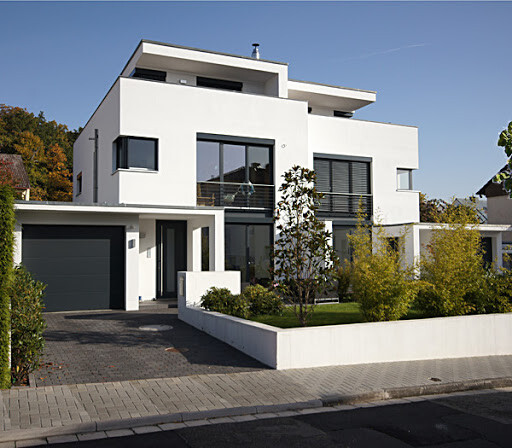 Moderne weiße Villa mit großen Fensterfronten, Garage links und gepflegtem Vorgarten.