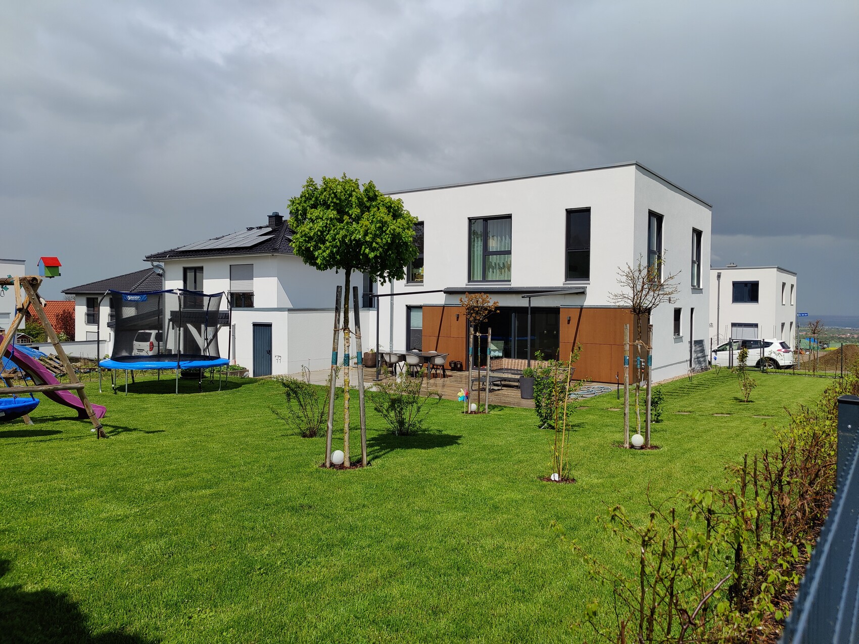 Modernes weißes Wohnhaus mit Terrasse, großem Garten und Trampolin-Spielbereich.