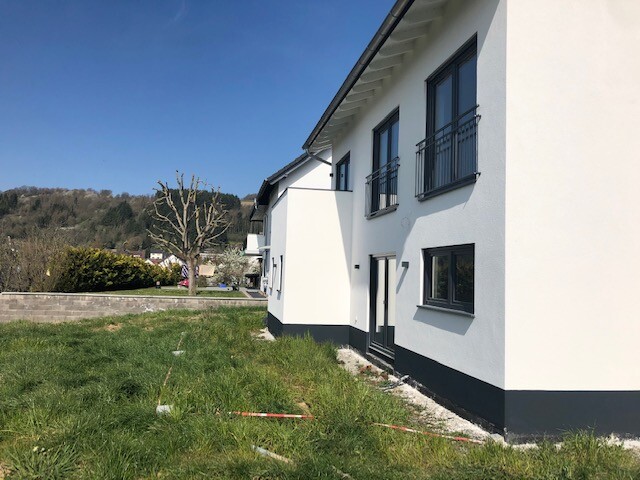 Moderne weiße Häuserfront mit schwarzen Fenstern, grünem Rasen und blauem Himmel.
