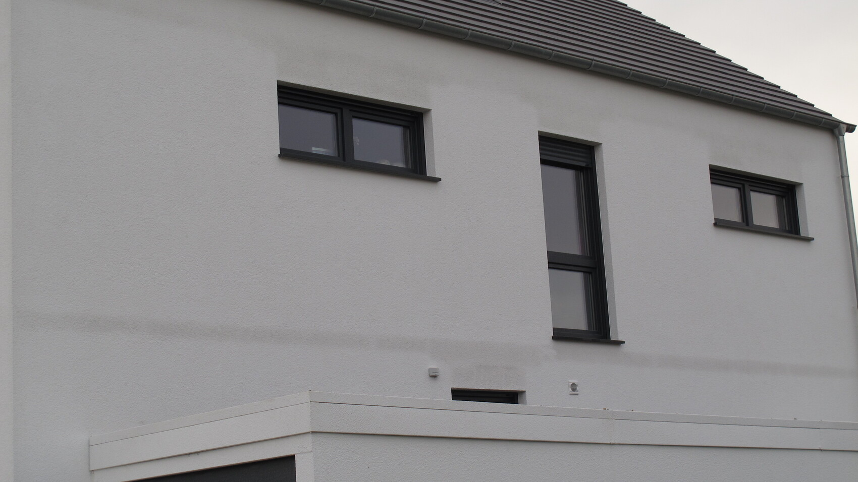 Weiße Fassade eines Hauses mit schwarzen Fensterrahmen und mehreren rechteckigen Fenstern