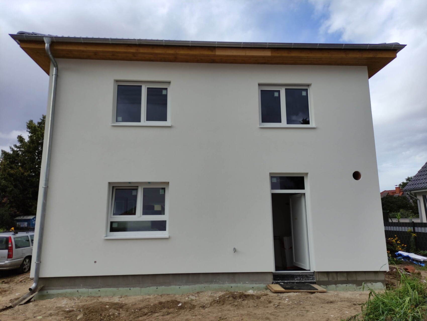 Zweistöckiges, weiß verputztes Haus auf Baustelle mit offener Tür und drei Fenstern.