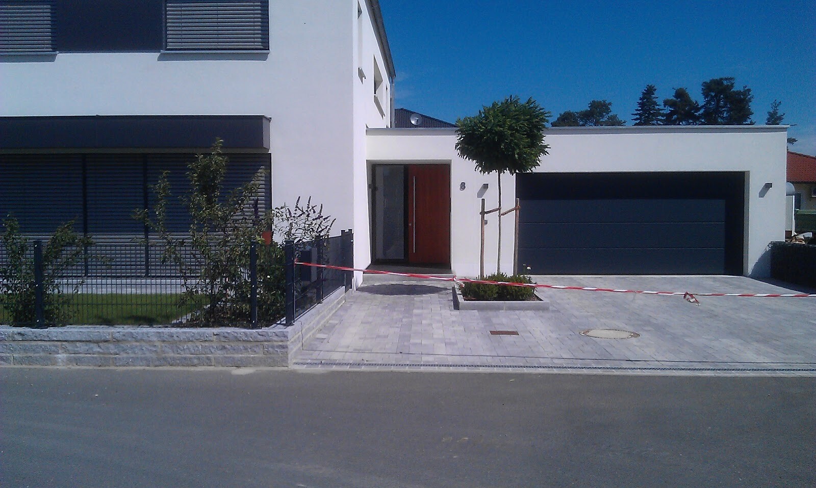 Modernes weißes Haus mit dunkler Garage, roter Eingangstür und Absperrband am Eingang.