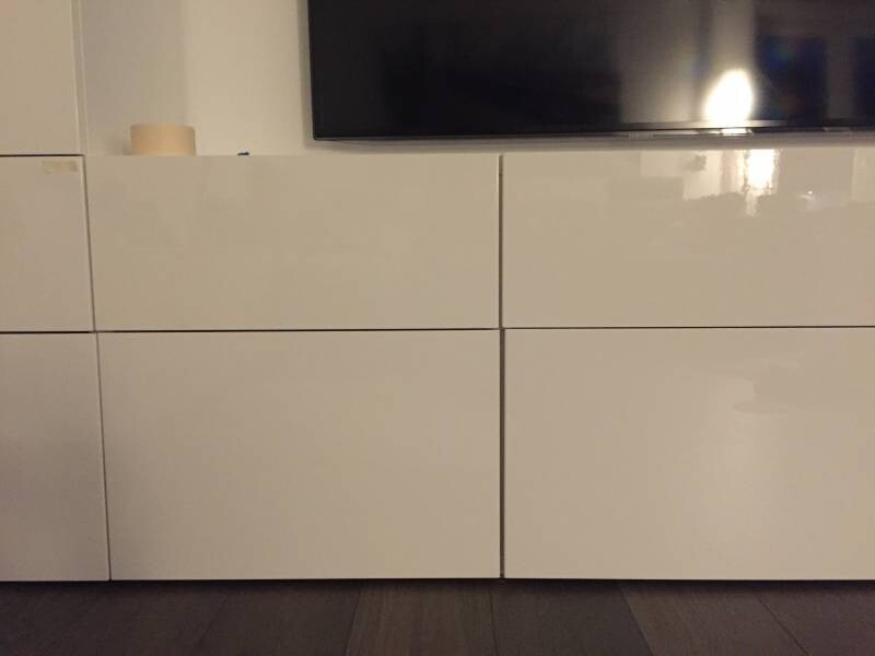 Weiße Hochglanz-Kommode mit Flachbildfernseher darauf, dunkler Boden.