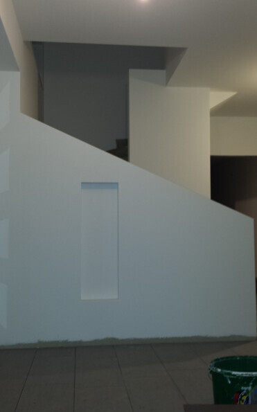 Weißer Innenraum mit schräger Wand, rechteckige Nische, dunkler Hintergrund und grünem Eimer.