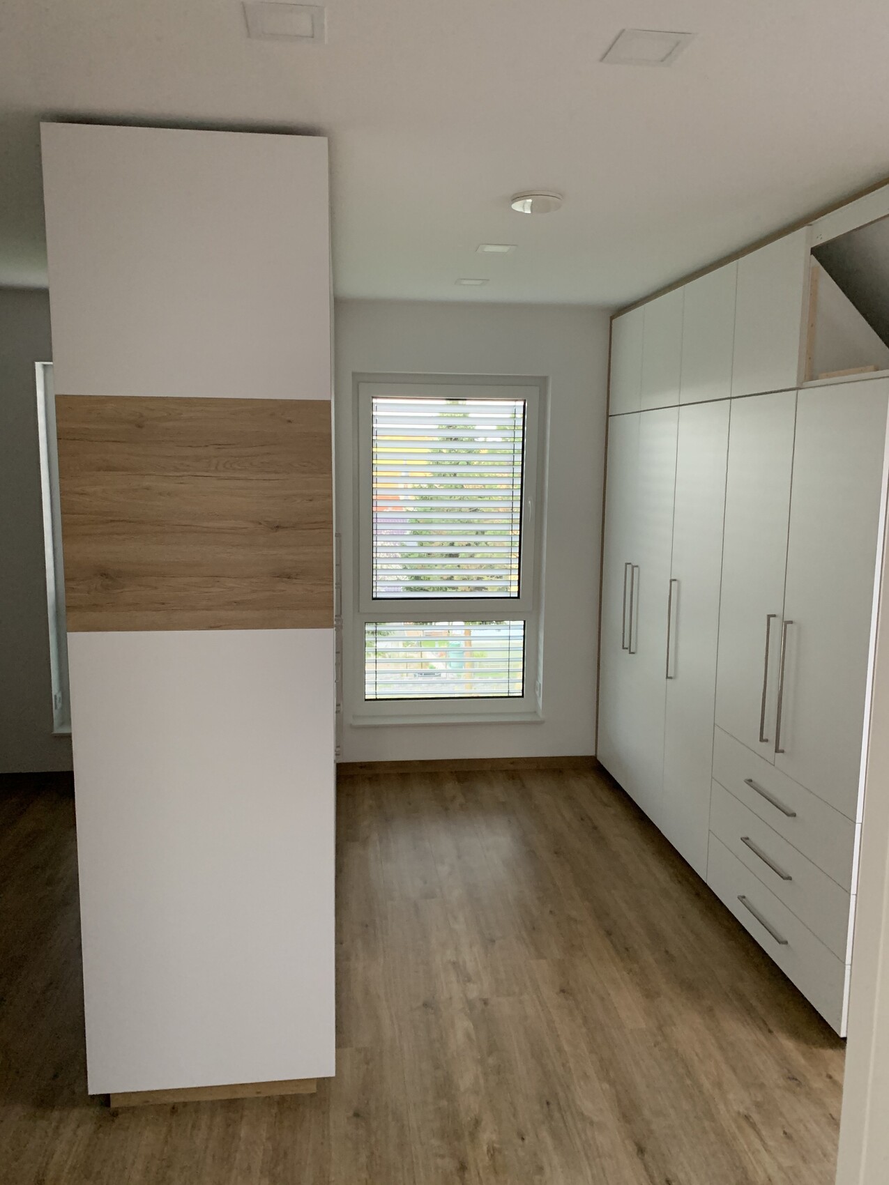 Moderne Küche mit hohem Schrank mit Holzstreifen, weiße Schränke rechts und Fenster mit Jalousien.