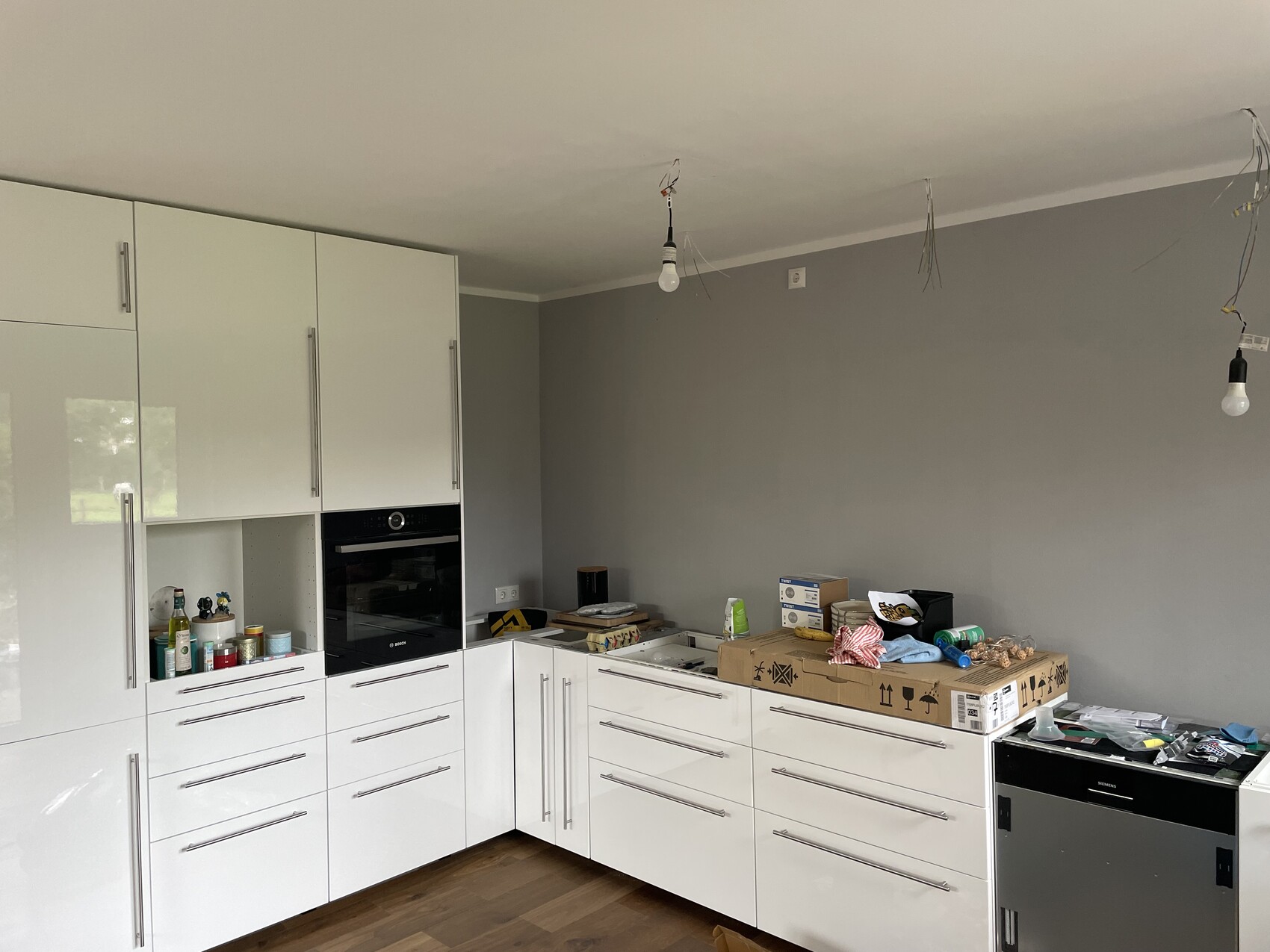 Moderne weiße Küche mit Backofen; Kartons, Reinigungsmittel und lose Kabel von der Decke hängen.
