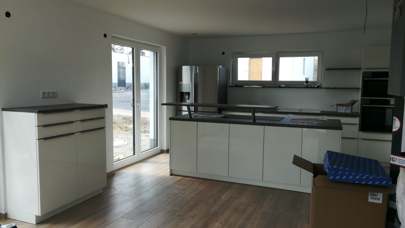 Moderne Küche mit weißen Hochglanzschränken, Insel, Edelstahlkühlschrank, Fenster.