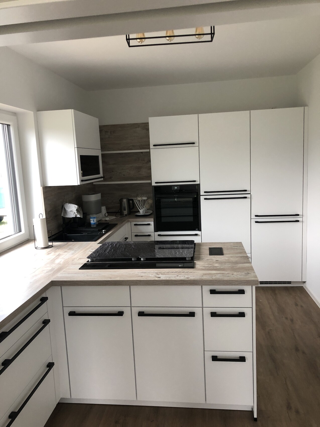 Moderne weiße Küche mit Holzarbeitsplatte, Insel mit Kochfeld, Backofen und Mikrowelle.