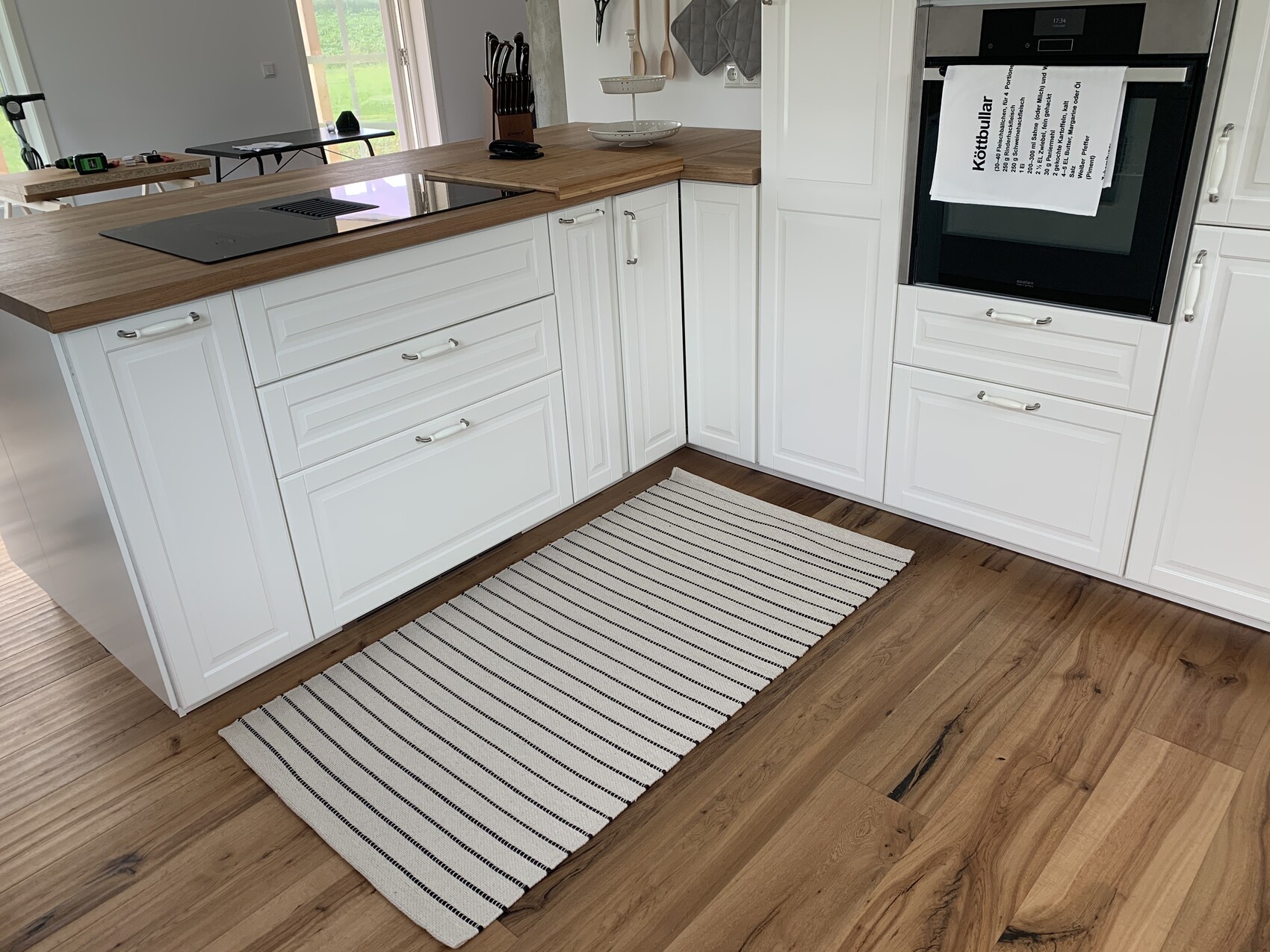 Moderne Küche mit weißen Schränken, Holz-Arbeitsplatten, Insel und Backofen; Holzboden.