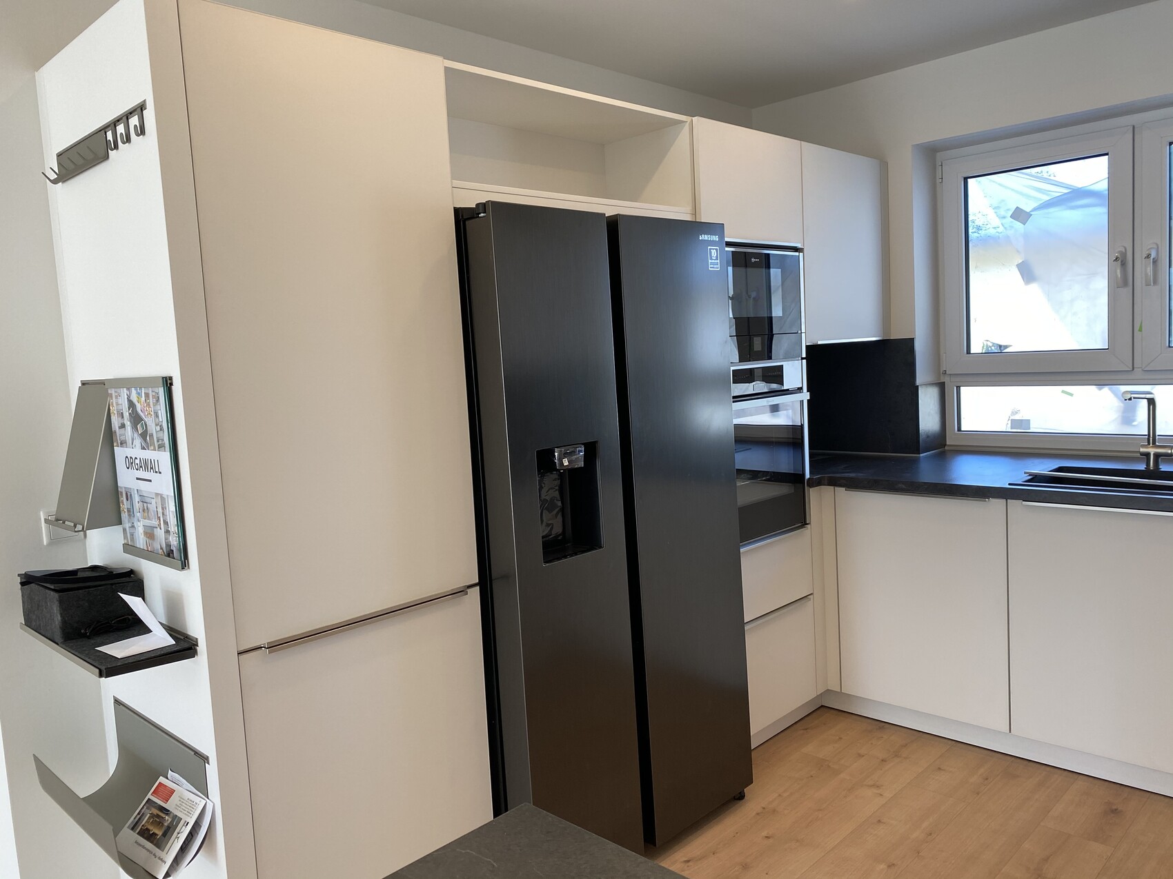 Moderne Küche mit weißen Schränken, Kühlschrank, Ofen-Kombi und Spüle am Fenster.