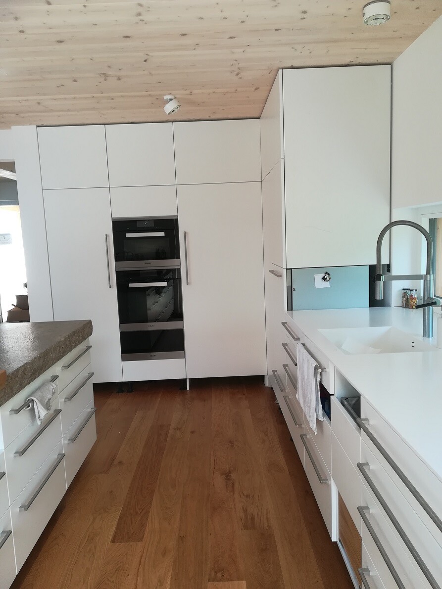 Moderne weiße Küche mit Doppel-Backofen, breiten Schränken, Holzfußboden und Spüle.