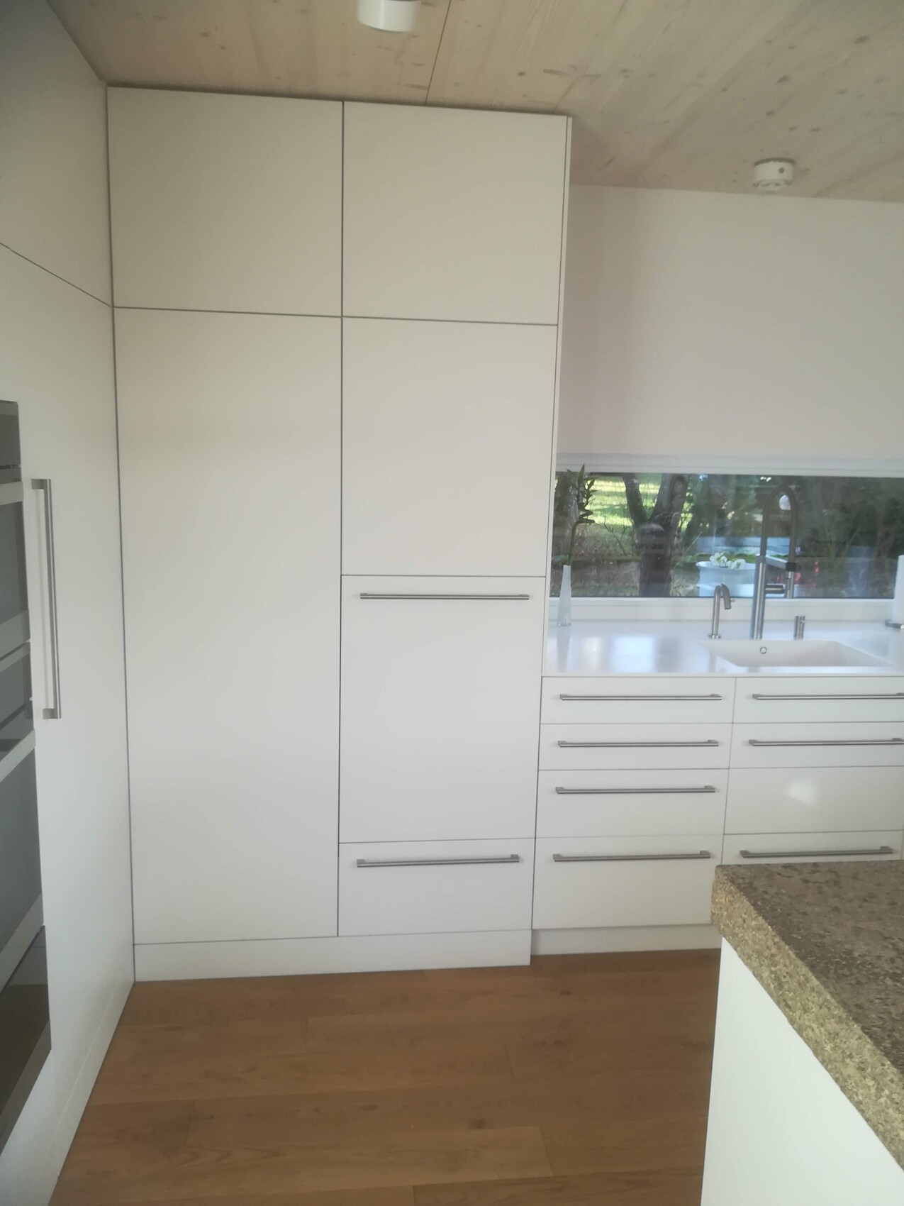 Moderne Küche mit weißen Schränken, Spüle am Fenster, Holzfußboden und Kücheninsel rechts.