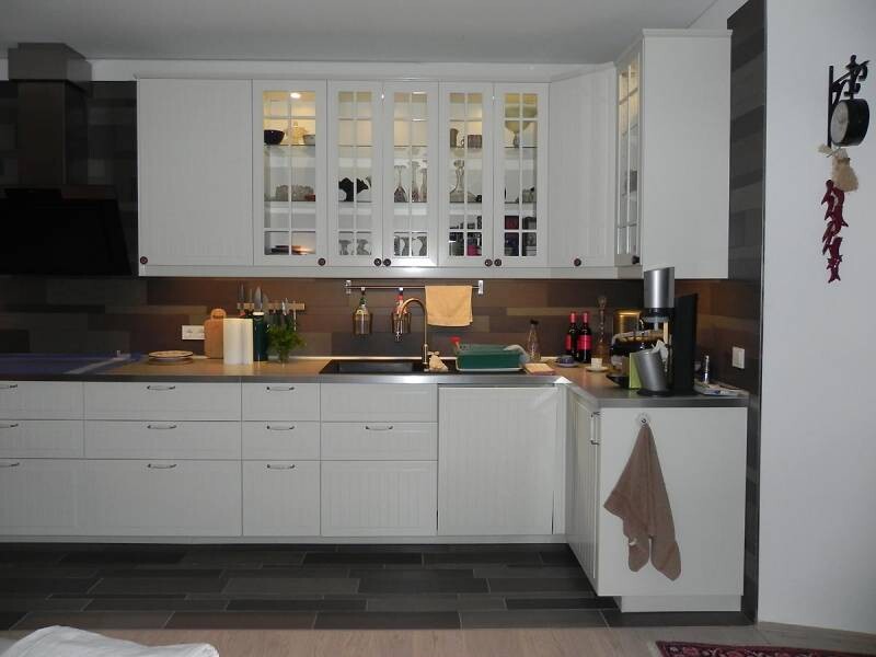 Moderne weiße Küche mit Glasfronten, Spüle und Kaffeemaschine rechts.